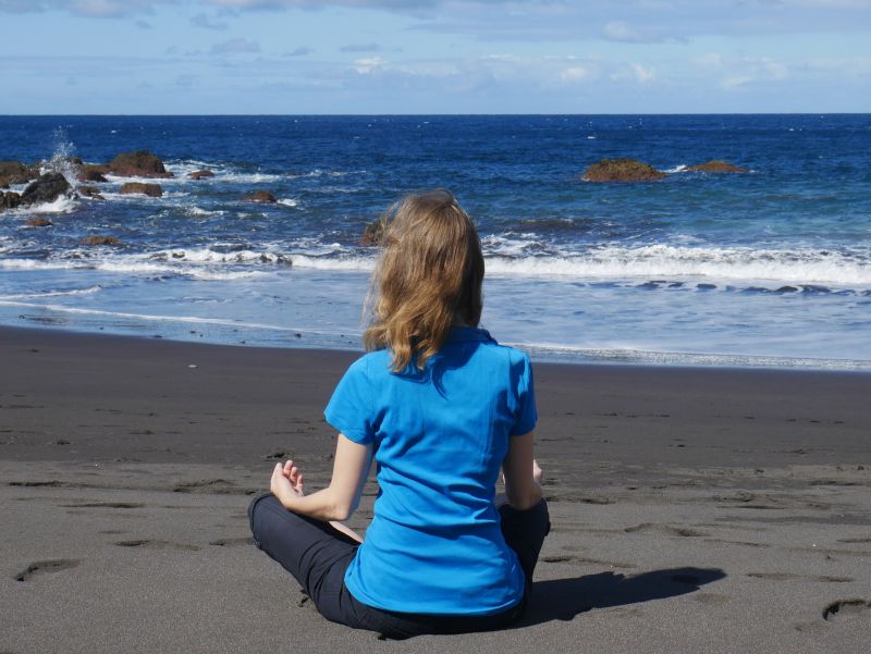 Eine Frau meditiert am Strand.
